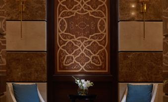 a luxurious living room with two blue armchairs , a wooden floor , and a large decorative wall hanging at Pullman Zamzam Madinah
