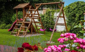 a wooden swing set with a slide in a lush green garden , surrounded by flowers at Villa Rosa