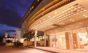 a modern hotel building with a curved entrance , lit up at night , and surrounded by trees at Hotel Ichibata