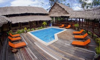 a wooden deck surrounding a swimming pool , with several lounge chairs and umbrellas placed around the pool area at Heliconia Amazon River Lodge