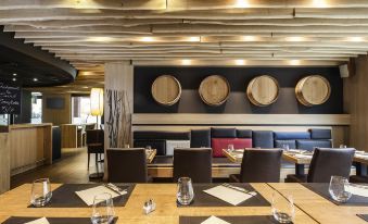 a restaurant with wooden tables and chairs , wine barrels on the wall , and hanging lights at Ibis Mulhouse Bale Aeroport
