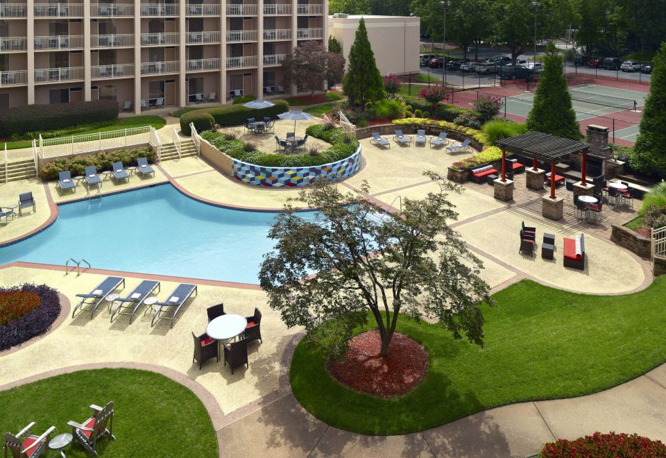 a large outdoor pool area with lounge chairs , tables , and umbrellas , surrounded by a lush green lawn at Atlanta Airport Marriott