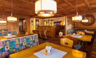 a cozy restaurant with wooden furniture , including a bar and dining tables , decorated with colorful tablecloths at Hotel Adler