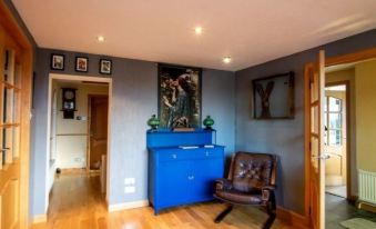 a living room with a blue dresser , wooden floor , and a black leather chair in the corner at Burnside Cottage