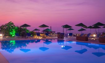 a large swimming pool with umbrellas and lounge chairs is illuminated by blue lights at dusk at Manolya Hotel