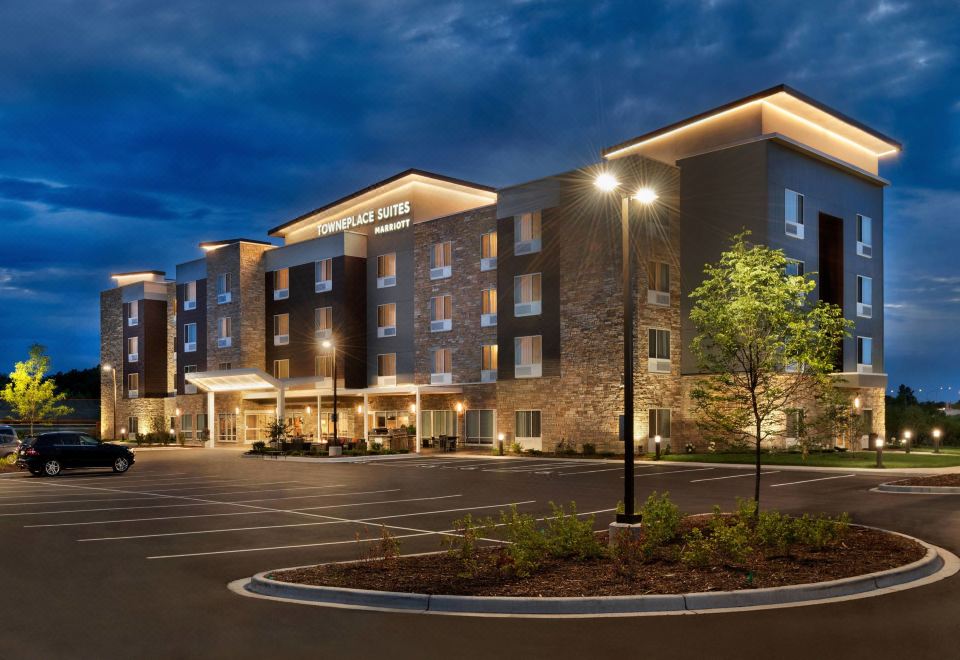 a modern hotel building with multiple floors , surrounded by trees and lit up at night at TownePlace Suites Milwaukee Grafton