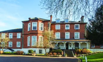 a large red brick building with white trim , surrounded by trees and a set of stairs leading up to the entrance at Brandshatch Place & Spa