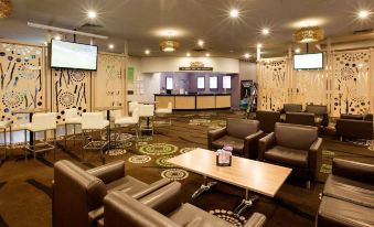 a large , modern lounge area with leather couches and chairs , wooden tables , and a bar at Nightcap at Waltzing Matilda Hotel