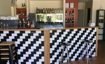 a modern bar with black and white checkered walls , wooden counter , and stools , as well as several bottles of wine on the counter at Myrtleford Motel on Alpine