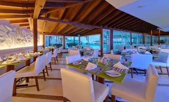 a restaurant with white chairs and tables , wooden ceiling , and large windows overlooking the ocean at Hotel Dann Cartagena