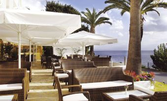 a beach - side terrace with white umbrellas , lounge chairs , and tables , providing a pleasant atmosphere for guests at Louis Ionian Sun