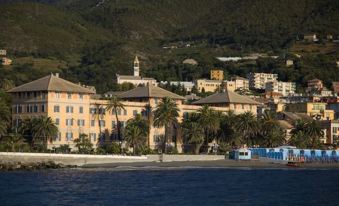 a picturesque coastal town with buildings and palm trees , set against the backdrop of mountains and water at Grand Hotel Arenzano