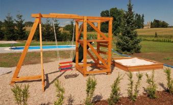 a wooden swing set with a bench and slide , situated in a grassy field near a swimming pool at Filip
