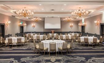 a large conference room with multiple tables and chairs , a projector screen , and chandeliers hanging from the ceiling at The Equinox