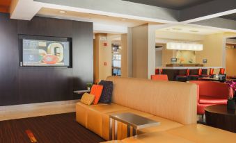a modern hotel lobby with a large couch and a tv , creating a comfortable space for guests at Courtyard Flint Grand Blanc