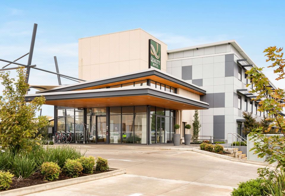 a large building with a green sign on the front , surrounded by trees and grass at Quality Hotel Rules Club Wagga