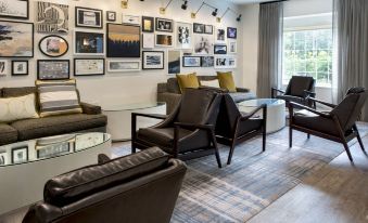 a modern living room with two brown leather chairs , a glass coffee table , and framed pictures on the wall at Delta Hotels Basking Ridge