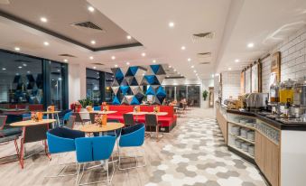 a modern restaurant with a dining area featuring blue and red chairs , tables , and a checkered floor at Holiday Inn Express Stockport