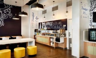 a modern coffee shop with a white counter , black pendant lights , and wooden furniture , attracting customers at Ibis Budget Auckland Airport