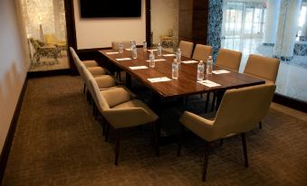 a conference room with a large wooden table , several chairs , and water bottles on the table at Hilton Garden Inn Dallas - at Hurst Conference Center