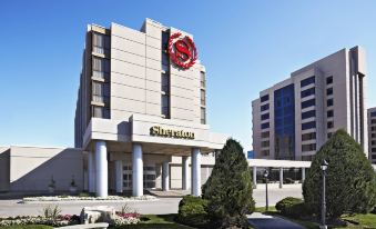 a large building with a red and white sign on top , surrounded by a park - like setting at Sheraton Parkway Toronto North Hotel & Suites