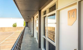 a long , narrow walkway with white columns and windows on one side , leading to a wooden fence at Nightcap at Westside Hotel