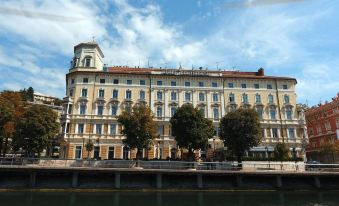 a large , ornate building situated on the banks of a river , with trees and people in the background at Hotel Continental