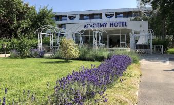 the exterior of the academy hotel , a white building with a blue sign and lush greenery surrounding it at Academy Hotel