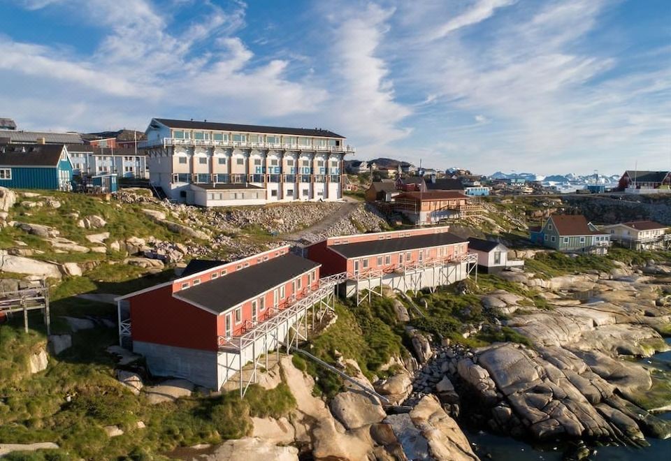 a group of buildings with red roofs on a rocky cliff , surrounded by water and mountains at Hotel Hvide Falk