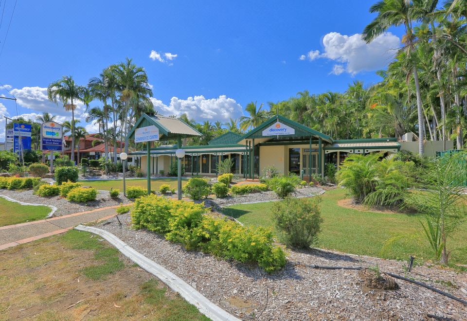 a house with a green roof and large windows is surrounded by tropical plants and bushes at Discovery Parks - Rockhampton