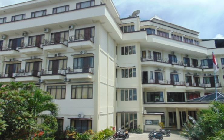 a large white building with multiple floors and balconies , surrounded by greenery and parked motorcycles at Hotel Grand Papua Fakfak