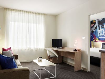 a living room with a couch , a coffee table , and a tv . also a chair in the room at Ibis Melbourne Hotel and Apartments