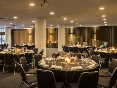 a large , well - lit dining room with multiple round tables set for a formal event , featuring black tablecloths and white napkins at Ibis Melbourne Hotel and Apartments