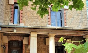 a brick house with blue shutters and a large tree in front of it , creating a picturesque scene at La Roseraie