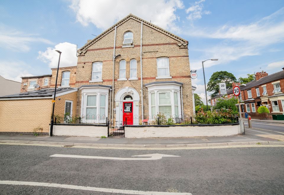 a two - story brick building with a red door , situated on a street corner in a residential area at Diamonds Villa Near York Hospital