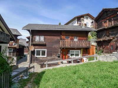 a wooden house with a balcony and green grass in front of it , situated on a hillside at Marilyn Visperterminen