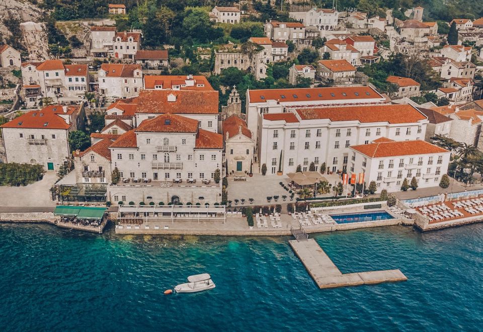 aerial view of a large white building situated on the edge of a body of water , with a boat docked nearby at Heritage Grand Perast by Rixos