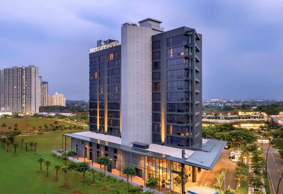 a tall hotel with a parking lot and greenery in front of it , under a cloudy sky at Mercure Tangerang BSD City