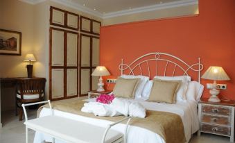 a large bed with white and beige linens is in a room with an orange wall at Villanova