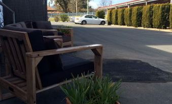 a wooden chair with a black cushion is placed on the side of a road , next to a potted plant at Cherry Blossom Motor Inn