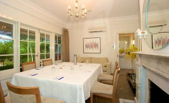 a dining room with a long white table surrounded by chairs , and a chandelier hanging from the ceiling at Brooklands of Mornington