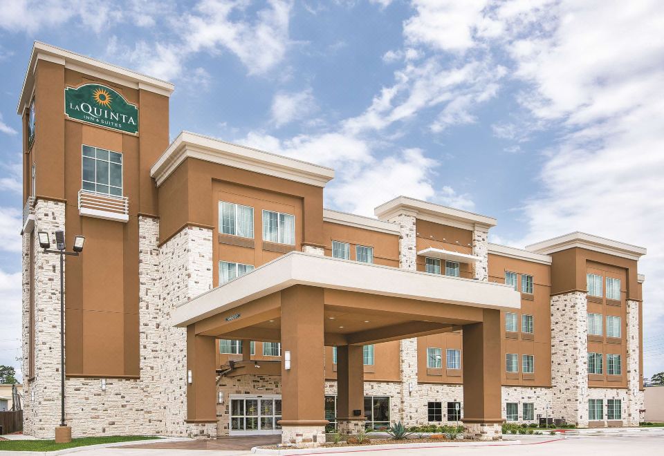 a large building with a brown facade and a stone archway entrance , under a clear blue sky at La Quinta Inn & Suites by Wyndham Houston Humble Atascocita