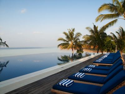 a row of blue and white striped lounge chairs lining a pool with palm trees in the background at Vilamendhoo Island Resort & Spa