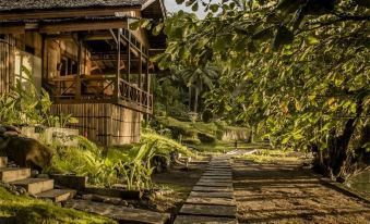 a wooden house surrounded by lush greenery , with a pathway leading up to the entrance at Janji Laut Resort