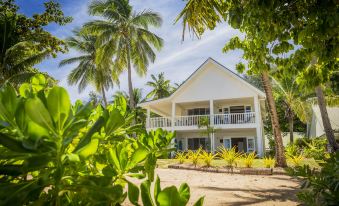 a beach house surrounded by palm trees and greenery , with the sun setting in the background at Malolo Island Resort