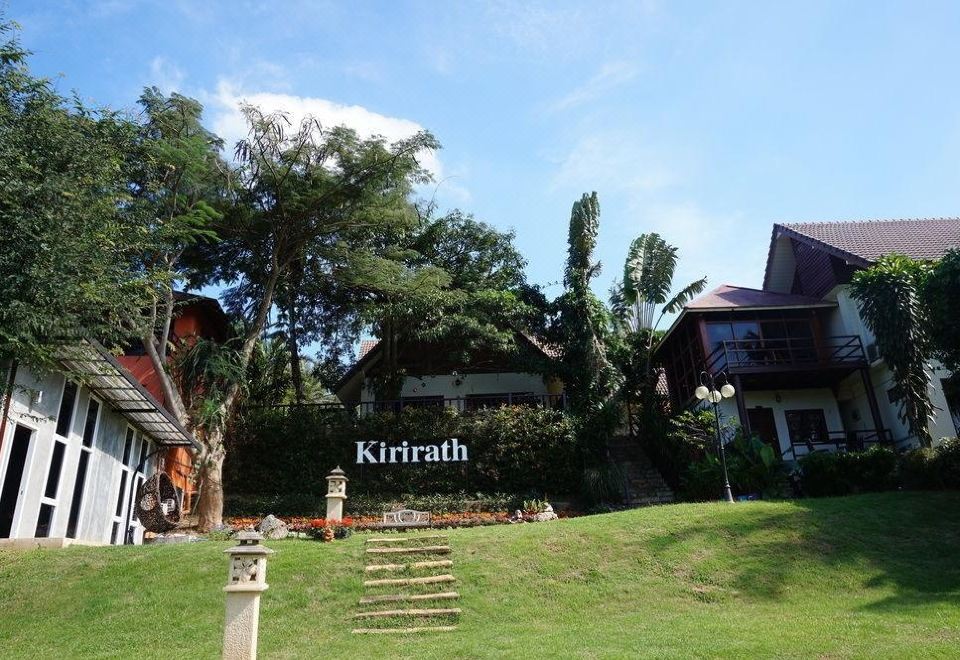 a large wooden house surrounded by a lush green lawn , with stairs leading up to the entrance at Kirirath Resort