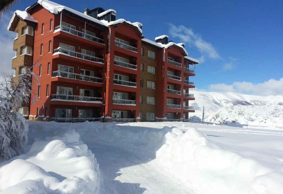 a large , red - brick building surrounded by snow - covered mountains , with a clear blue sky in the background at Village Condo