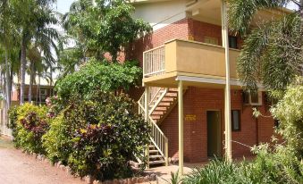 a red brick building with a staircase leading up to the second floor , surrounded by greenery at Litchfield Outback Resort