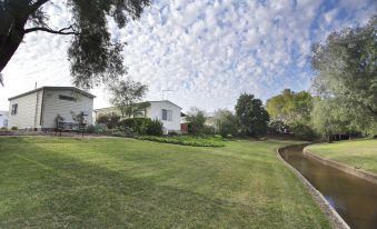 a large white house surrounded by a grassy yard , with a pond in the background at Discovery Parks - Perth Airport