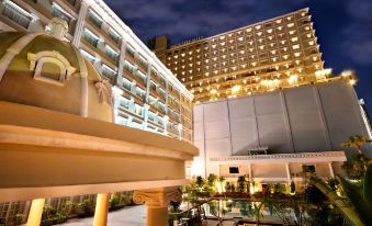 a tall building with many windows is lit up at night , surrounded by a courtyard at The Rich Jogja Hotel